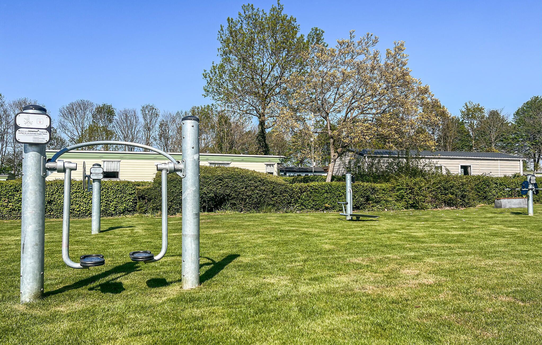 Une aire de jeux avec des balançoires et un toboggan, entourée d’herbe et d’arbres.