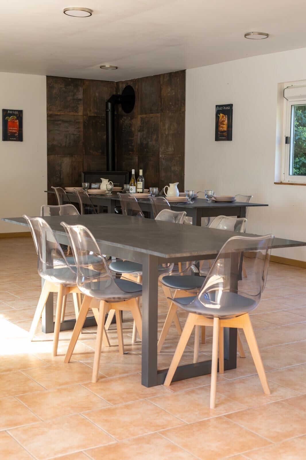 A modern dining area with a large rectangular table, clear plastic chairs, and a dark wooden accent wall.