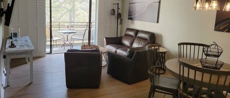 A spacious living area with a leather sofa, a dining table, and a balcony with a view.
