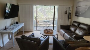 A living room with a sofa, chairs, a coffee table, a TV, and a balcony with a table and chairs. - Sunsets and Sand dunes (Myrtle Beach)