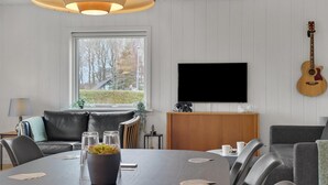 A modern living room with a dining area, a large window, a flat-screen TV, and a guitar. - Cozy home in Nykøbing M with WiFi (Nykøbing M)