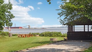 A picnic area with benches and a wooden structure, overlooking a body of water with industrial buildings in the background. - Cozy home in Nykøbing M with WiFi (Nykøbing M)