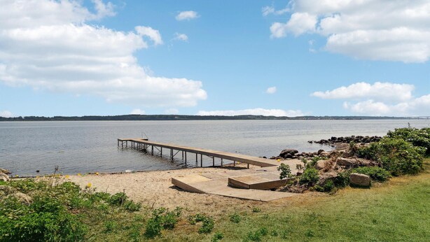 A wooden pier extending into calm water, surrounded by a grassy area with rocks and vegetation. - Cozy home in Nykøbing M with WiFi (Nykøbing M)
