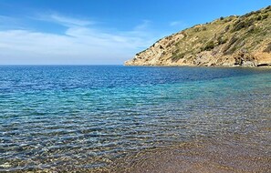 Une plage côtière aux eaux claires, avec un terrain rocheux et une mer calme.