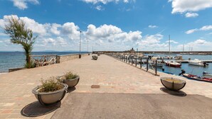 Een verharde promenade langs het water met stenen hekken, plantenbakken en uitzicht op boten in een jachthaven.