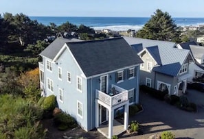A coastal house with a balcony, surrounded by greenery and a view of the ocean.