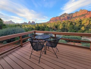 Un terrazzo in legno con tavolo e sedie che si affaccia su un paesaggio montuoso.
