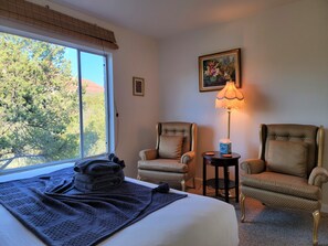 Una camera d'albergo con un letto, due poltrone, un tavolino con una lampada e un quadro appeso al muro.