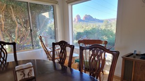 A dining area with a large table and chairs, a small cabinet, and a view of red rock formations through large windows. - Magnificent Sedona Redrock Views; 7-Min Walk to Uptown;Single-Level;Eco-Friendly (Sedona)