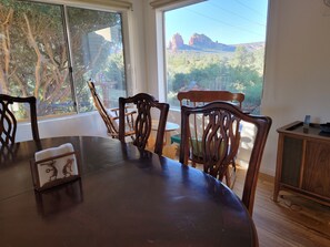 Ein Essbereich mit großem Tisch und Stühlen, einer kleinen Kommode und Blick auf rote Felsformationen durch große Fenster.