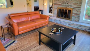 A living room with a leather sofa, a black coffee table, and a stone fireplace. - Magnificent Sedona Redrock Views; 7-Min Walk to Uptown;Single-Level;Eco-Friendly (Sedona)