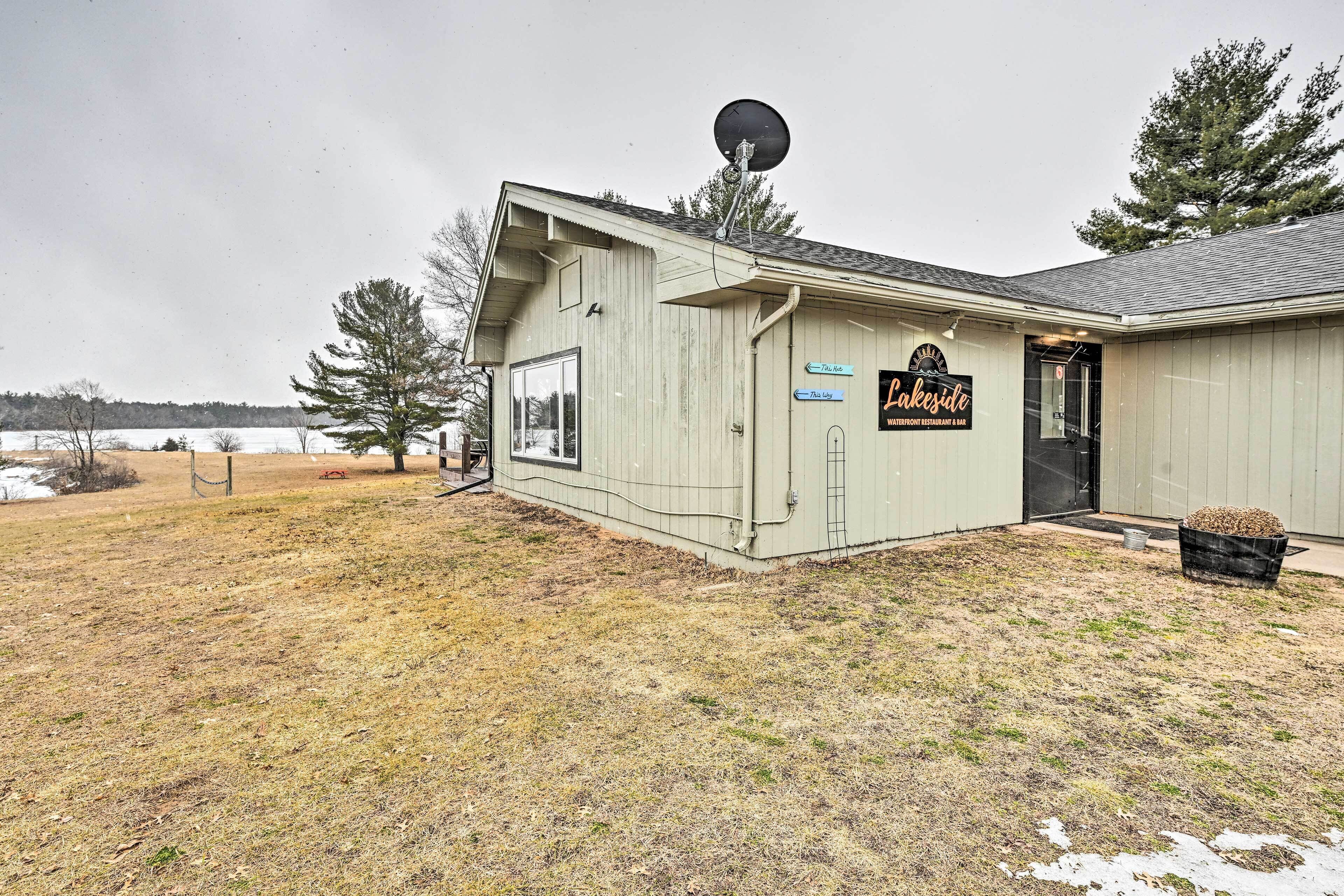 A lakeside building with a satellite dish, a sign reading "Lakeside Waterfront Restaurant & Bar," and a small outdoor seating area.