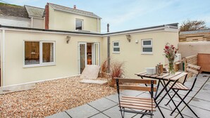 A patio with a table and chairs, a small garden area with pebbles, and a building with windows and a door. - 3 bedroom accommodation in St Austell (St Austell)