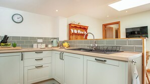 A modern kitchen with light green cabinets, a wooden countertop, a sink with a dish rack, and a clock on the wall. - 3 bedroom accommodation in St Austell (St Austell)
