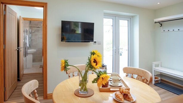 A modern bathroom with a shower, toilet, and sink. There is a TV mounted on the wall and a window with a view of the outside. - 3 bedroom accommodation in St Austell (St Austell)