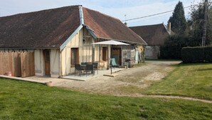 A rustic building with a sloped roof, a patio with outdoor seating, and a gravel driveway. - La Louvière - JEUGNY - Gîte (JEUGNY)