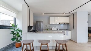 Une cuisine moderne avec des armoires blanches, un réfrigérateur en acier inoxydable et un four encastré. On y trouve trois tabourets en bois et une plante en pot.