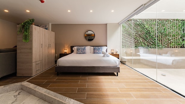 Une chambre moderne avec un grand lit, une armoire en bois et un mur de verre donnant sur un paysage verdoyant.