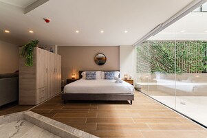 Une chambre moderne avec un grand lit, une armoire en bois et un mur de verre donnant sur un paysage verdoyant.
