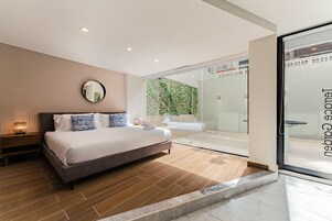 Une chambre moderne avec un grand lit, une table de chevet avec une lampe et une porte-fenêtre coulissante donnant sur un balcon.