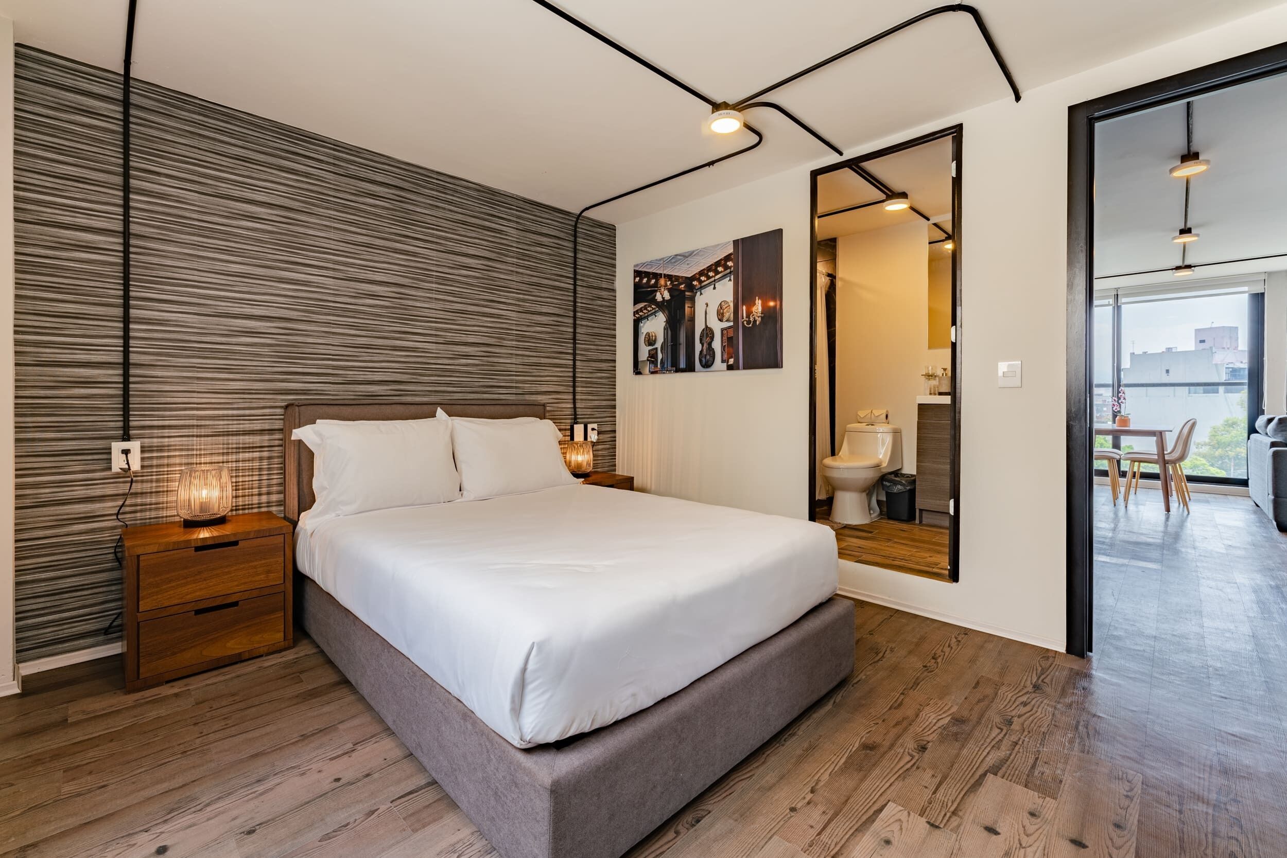Une chambre moderne avec un grand lit, une tête de lit en bois et une table de chevet avec une lampe.