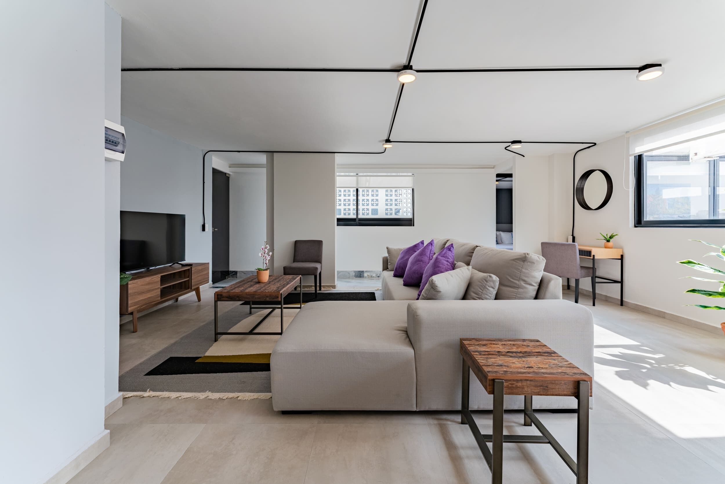 Een moderne woonkamer met een bank, salontafel en televisie. Een raam zorgt voor natuurlijk licht en uitzicht op de stad.