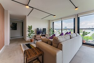 Un salon moderne avec un canapé, un téléviseur et de grandes fenêtres donnant sur la ville.