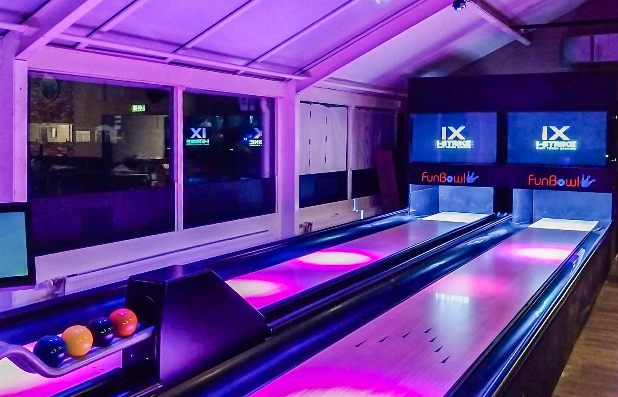 A bowling alley with multiple lanes, neon signage, and a row of colorful bowling balls.