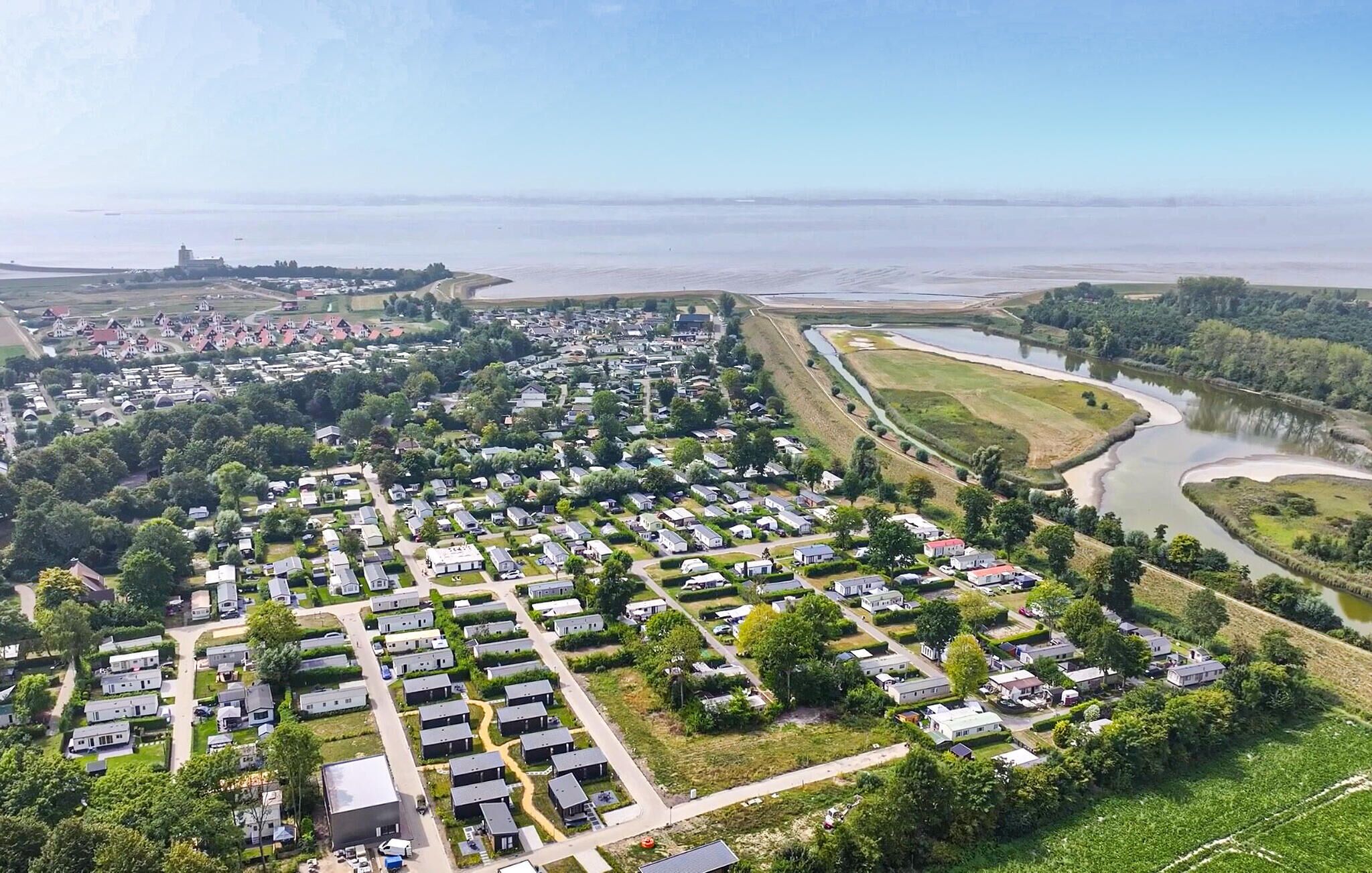 An aerial view of a campground with RVs and mobile homes, surrounded by greenery and a river.