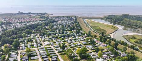 An aerial view of a campground with RVs and mobile homes, surrounded by greenery and a river.