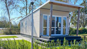 Une maison mobile moderne, de plain-pied, avec un toit plat, de grandes fenêtres et une véranda couverte.