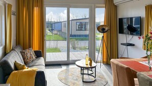 Un salon moderne avec un canapé, une table basse et un téléviseur. Il y a une grande fenêtre avec des rideaux, et un appareil de climatisation fixé au mur.