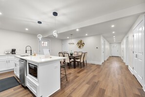 Une cuisine moderne avec des meubles blancs, un îlot central et un coin repas agrémenté d’un lustre.