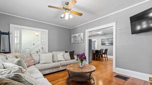 A living room with a grey sofa, a round coffee table with a vase, a ceiling fan, and a TV mounted on the wall. - Timelessly restored home - entirely yours to enjoy (Billings)