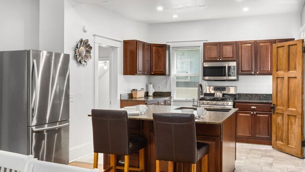 A modern kitchen with stainless steel appliances, wooden cabinets, and a dining area with two chairs. - Timelessly restored home - entirely yours to enjoy (Billings)