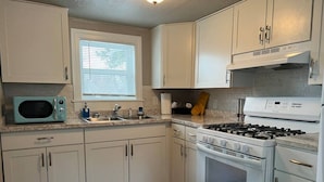 A kitchen with white cabinets, a microwave, a stove, and a window with blinds.