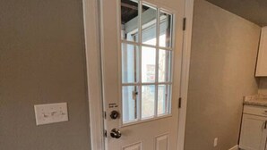 A room with a white door, a small cabinet, and a vent on the wall.
