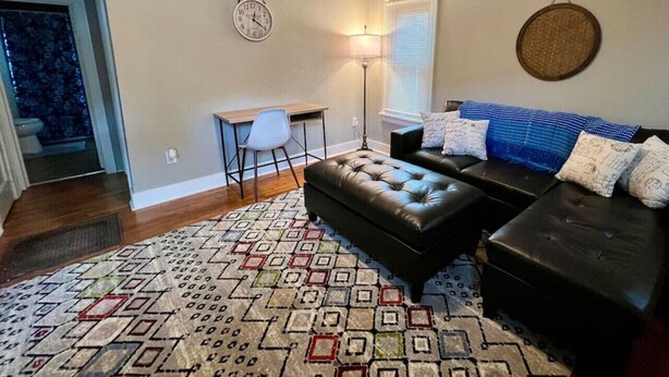 A living room with a patterned rug, a black leather sofa, a small table with chairs, and a lamp.