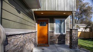 Une maison avec une façade en pierre, une porte d’entrée en bois et une fenêtre avec des stores.