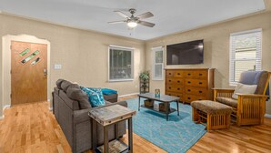 Un salon avec un ventilateur de plafond, un téléviseur, un canapé, une table basse, un fauteuil et un meuble en bois.