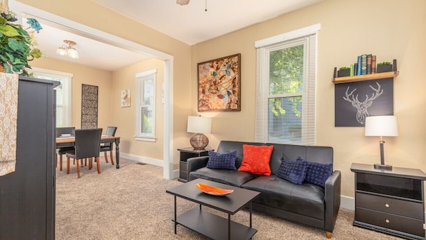 A living room with a black leather sofa, a coffee table, and a dining area with a table and chairs.
