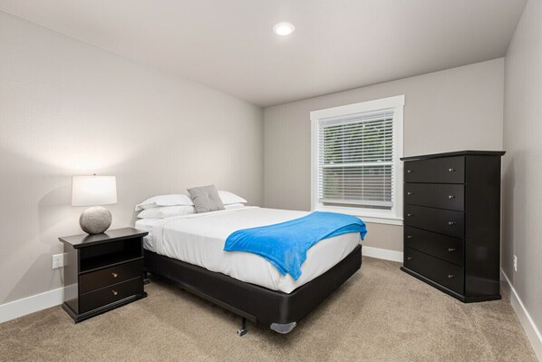 A bedroom with a bed, a nightstand, a dresser, and a window with blinds. - Delightful, new townhome downtown (Billings)