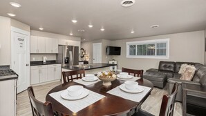 Una cocina moderna con armarios blancos, una mesa de comedor con platos blancos, y un sofá negro en la sala.