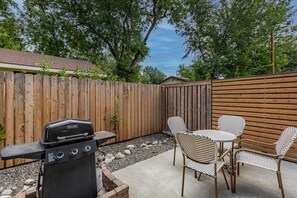 Un jardin avec une clôture en bois, un barbecue et une table avec des chaises.