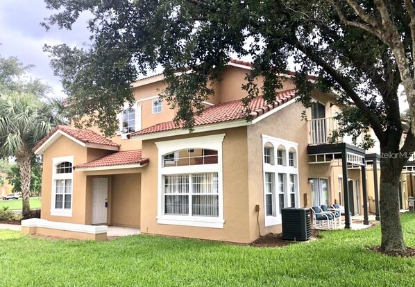 A two-story house with a red-tiled roof, a front porch, and a covered outdoor seating area.
