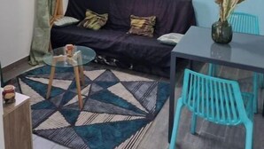 A living room with a dark blue sofa, a glass coffee table, a patterned rug, a painting of palm trees, and teal chairs. - Property in peaceful, central countryside (Ducos)