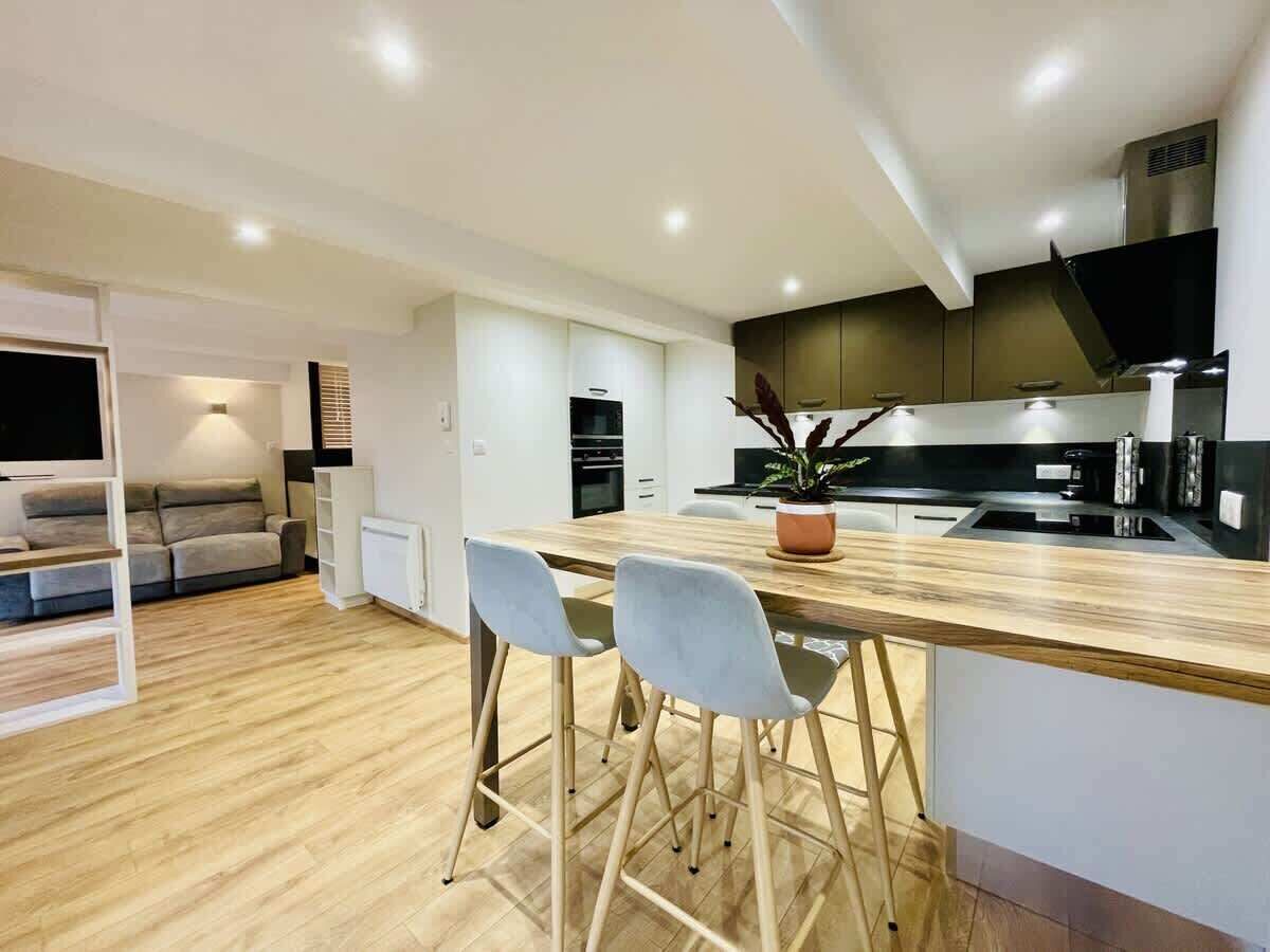 A modern kitchen with a wooden countertop, two bar stools, a potted plant, and a built-in oven.