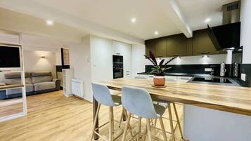 A modern kitchen with a wooden countertop, two bar stools, a potted plant, and a built-in oven.