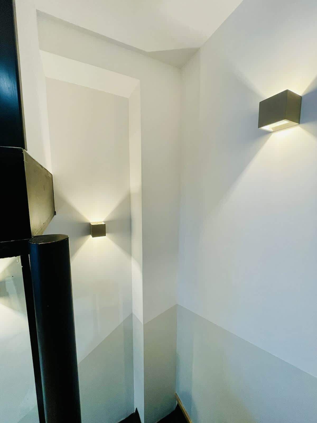 Un interno moderno dal design minimalista, caratterizzato da un angolo illuminato da un faretto incassato e da un elegante pilastro nero.