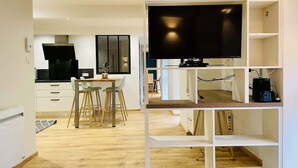 Ein moderner Wohnraum mit Küche, Essbereich und Fernseher auf einem weißen Regal.